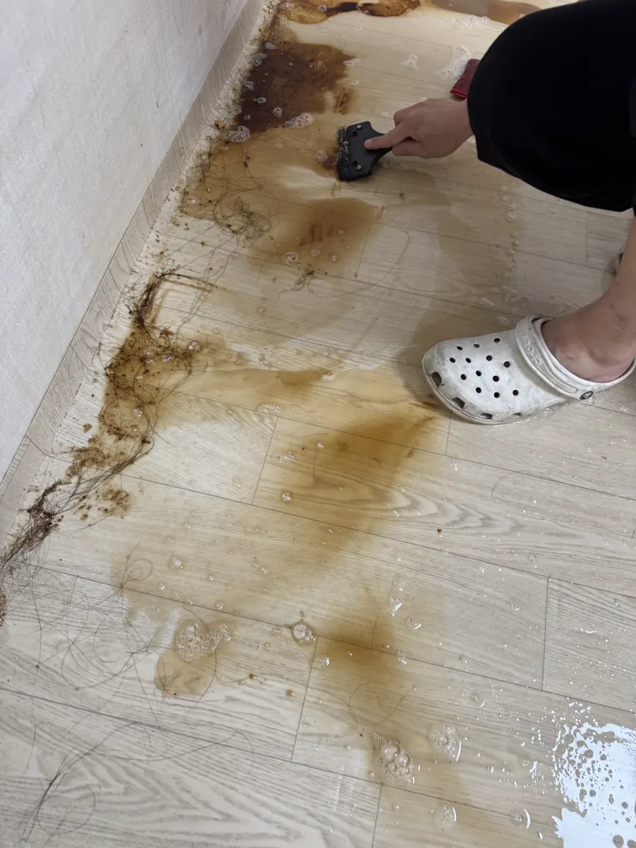 안산 원룸 바닥에 눌어붙은 얼룩을 스크래퍼로 긁어내는 모습